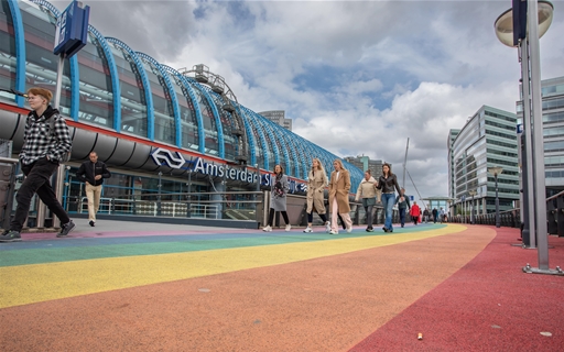 Voetgangers lopen over voetpad in regenboogkleuren bij station Sloterdijk in Amsterdam